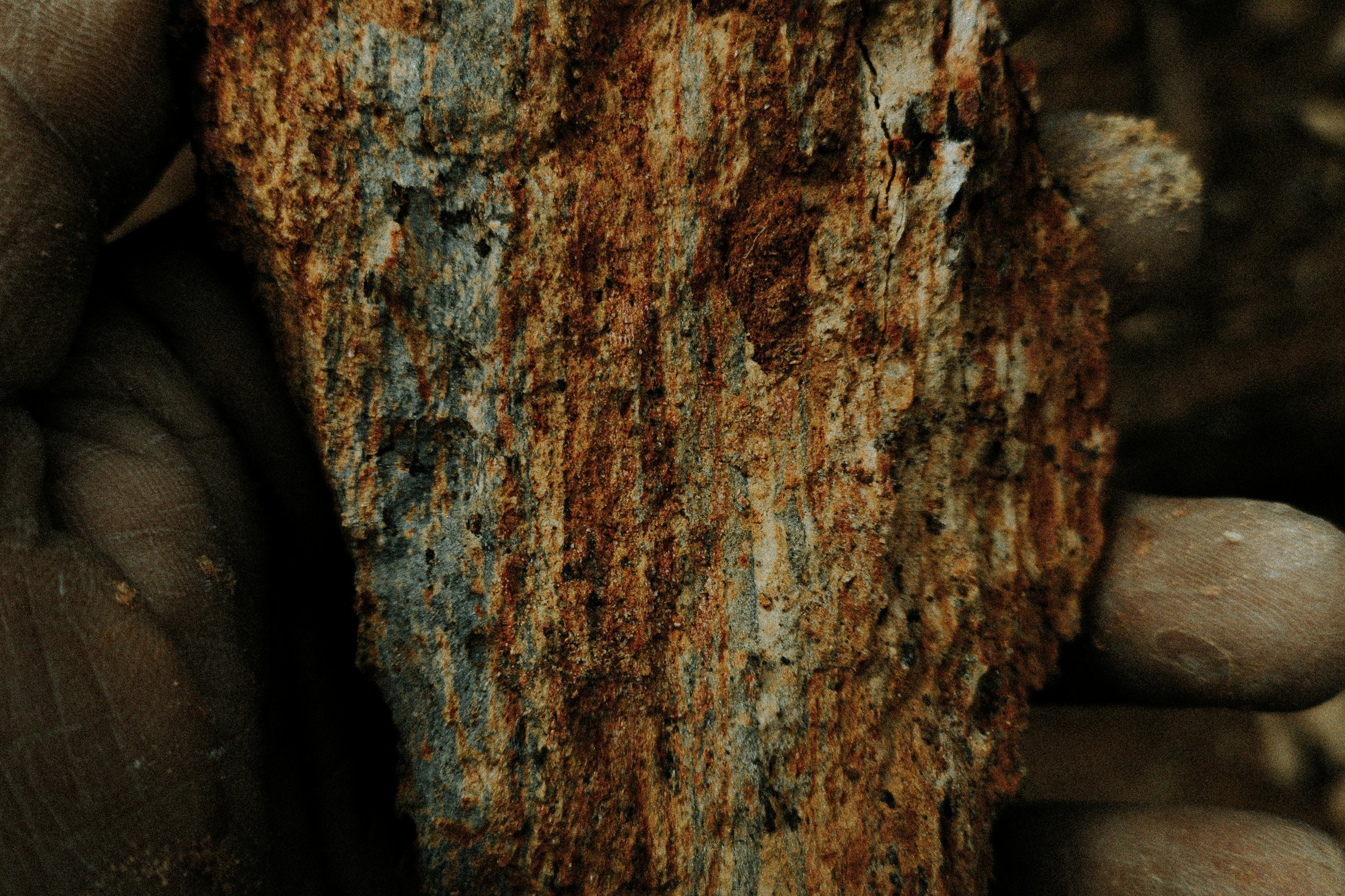 A hand holding a rough, rust-colored mineral specimen